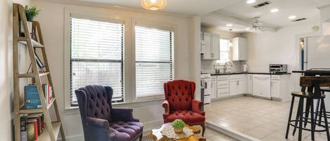 A modern kitchen with white cabinets, a red chair, a purple chair, and a wooden ladder with books.