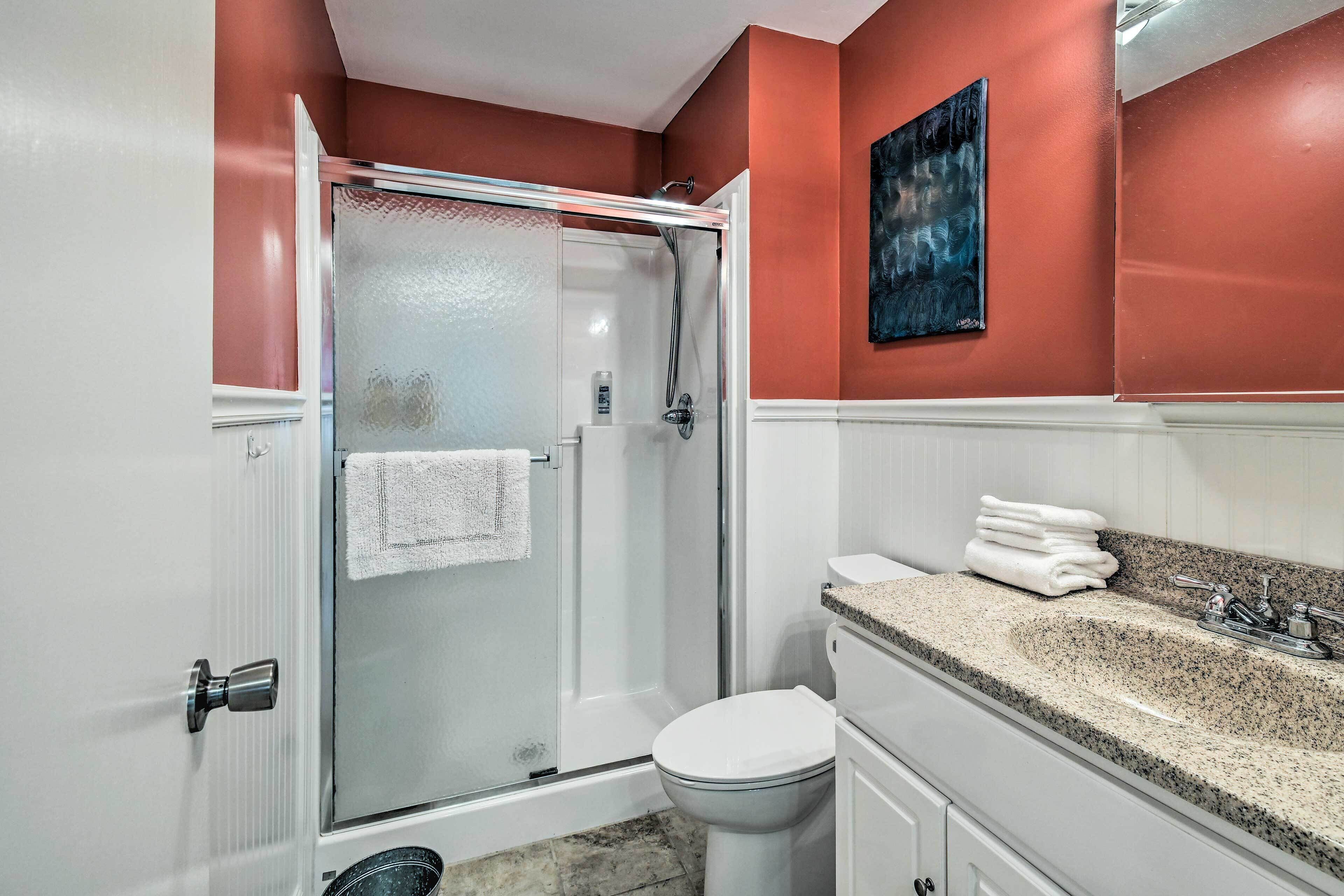 A bathroom with a glass-enclosed shower, white toilet, and granite countertop sink.