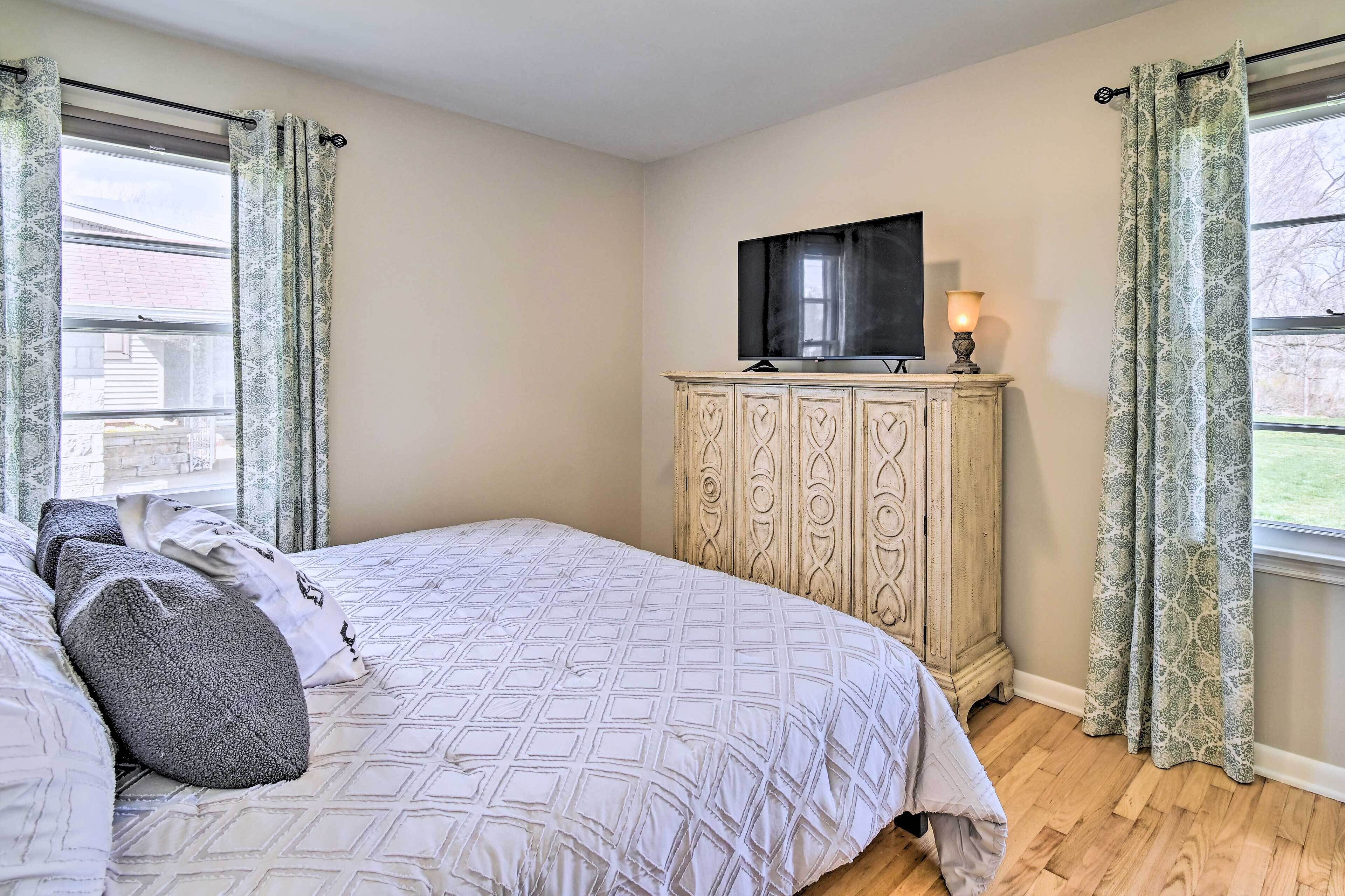 A bedroom with a bed, a TV on a cabinet, and curtains on the windows.