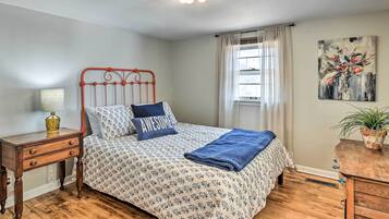 A bedroom with a bed, a nightstand, a lamp, a window with curtains, and a painting on the wall.
