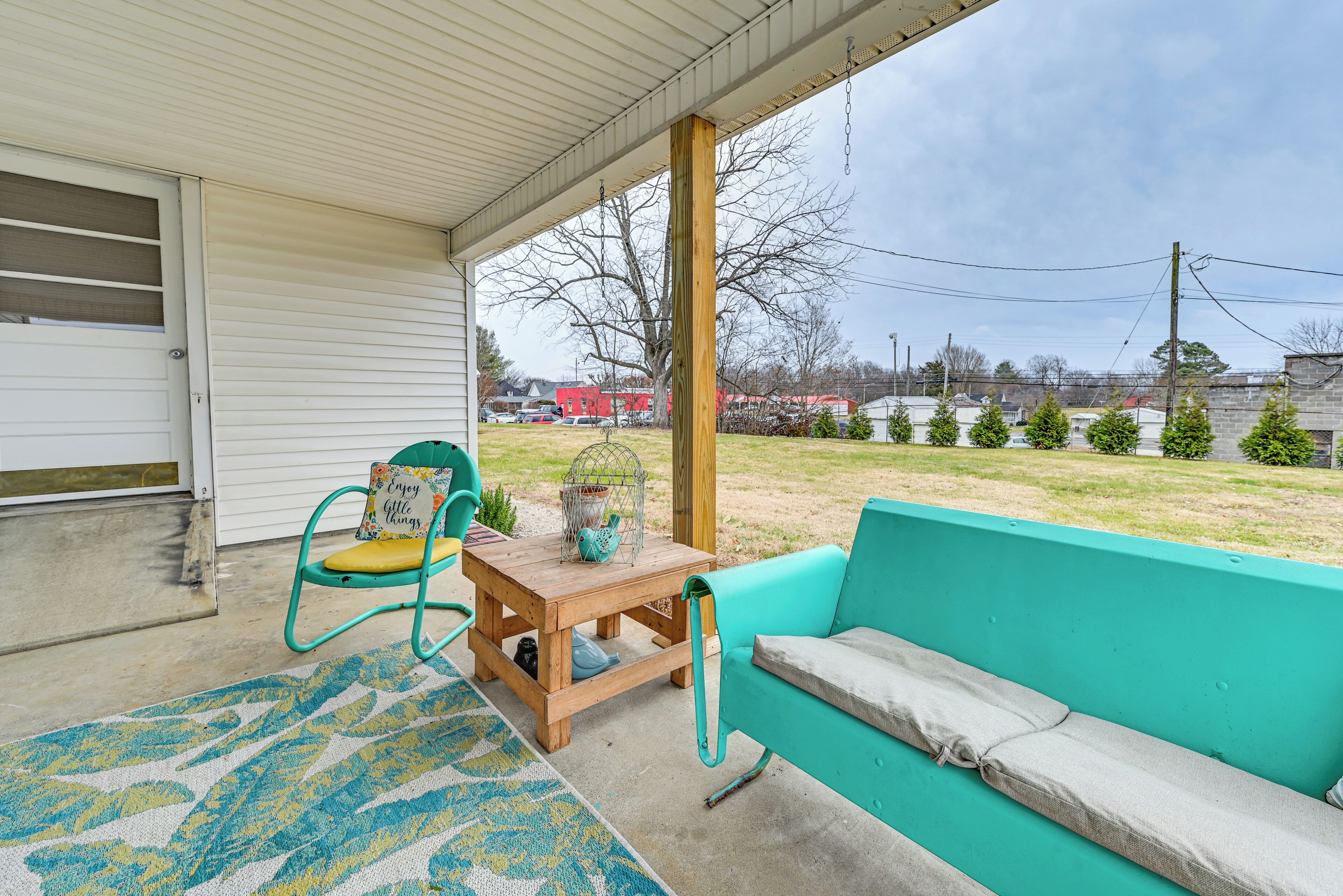 A covered porch with a wooden table, turquoise sofa, and teal chairs.