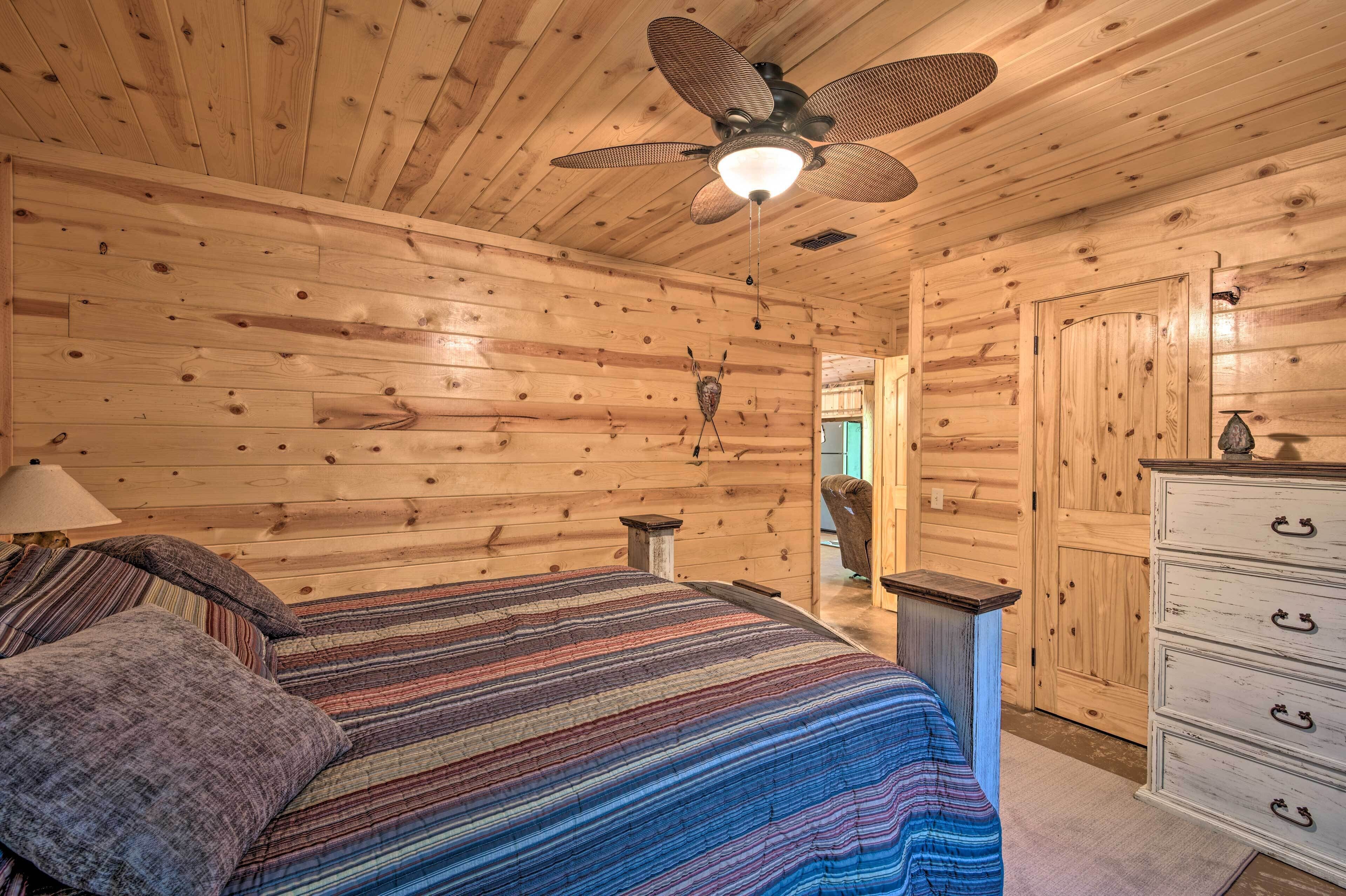 A wooden cabin bedroom with a bed, a dresser, a ceiling fan, and a door.