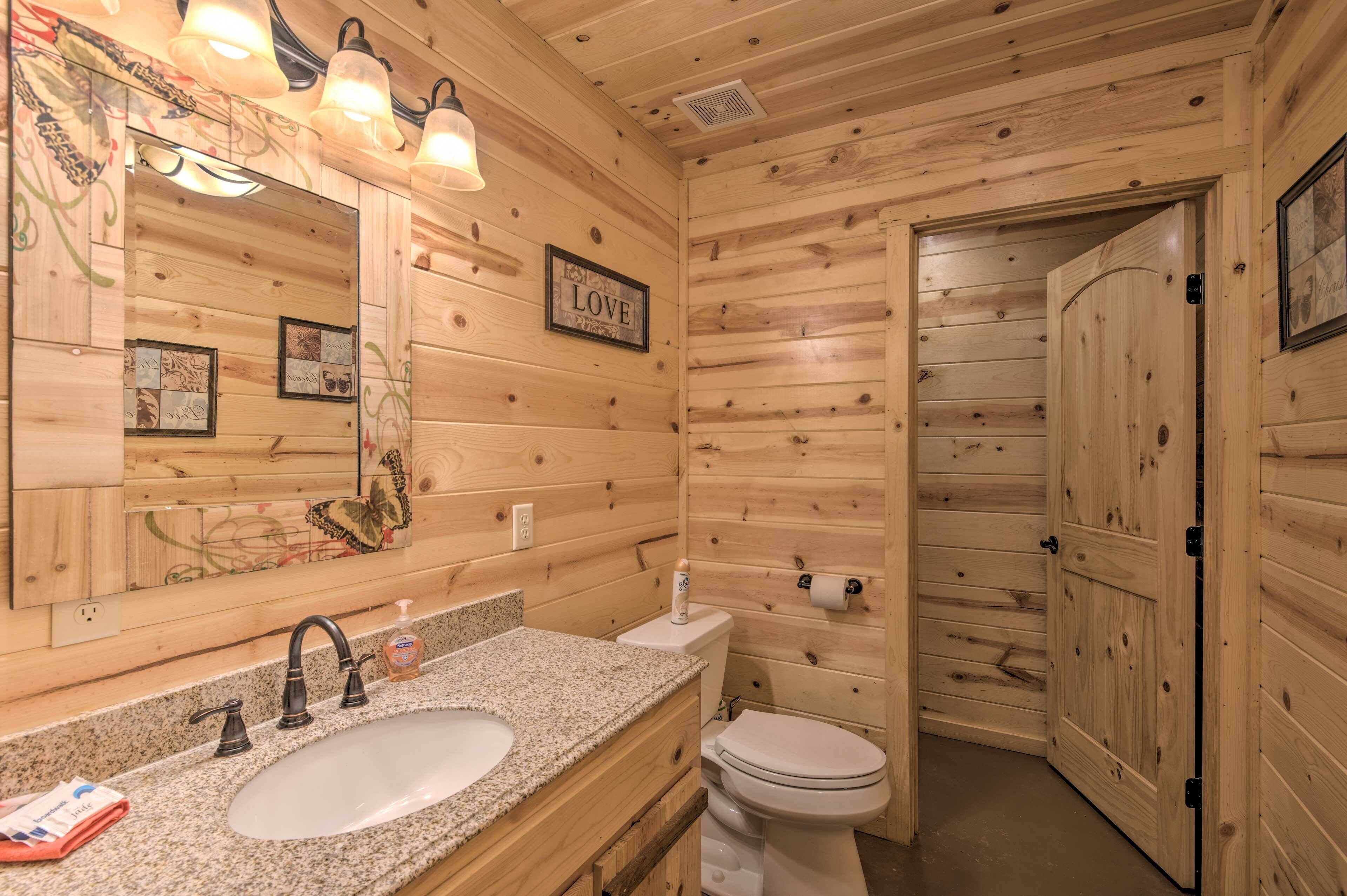 A wooden cabin bathroom with a sink, toilet, and a mirror with a 'LOVE' sign.