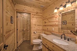 A wooden-paneled bathroom with a sink, toilet, and mirror. - Cabin w/ Hot Tub - Near Broken Bow Lake & Hiking! (Broken Bow)