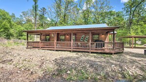 A wooden cabin with a porch, surrounded by trees and a stream. - Cabin w/ Hot Tub - Near Broken Bow Lake & Hiking! (Broken Bow)