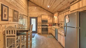 A wooden cabin kitchen with a dining table, chairs, a refrigerator, a microwave, an oven, and wooden cabinets. - Cabin w/ Hot Tub - Near Broken Bow Lake & Hiking! (Broken Bow)
