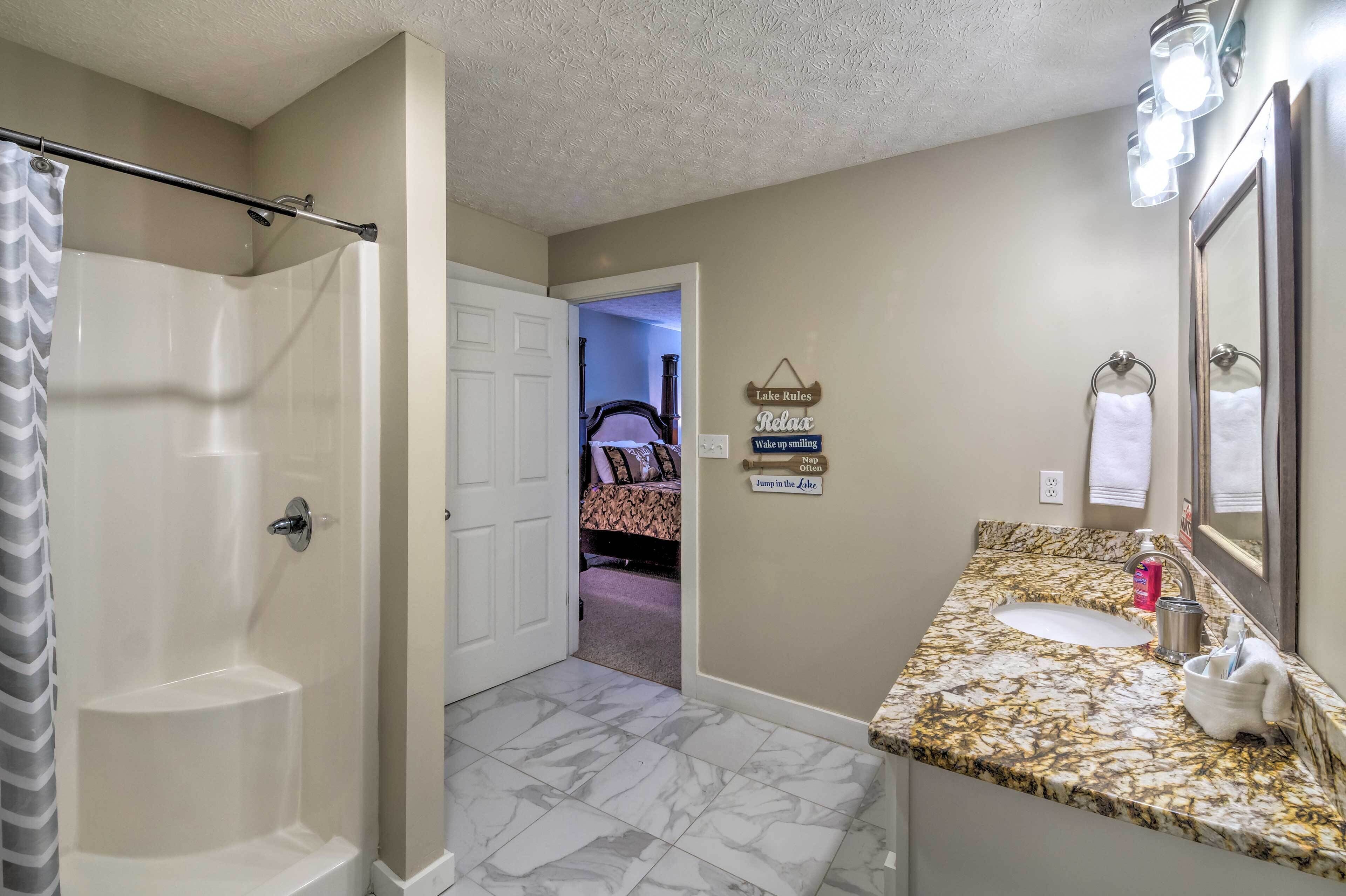 A bathroom with a shower, a sink with a marble countertop, and a mirror.