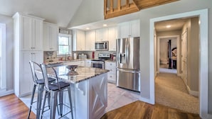 A modern kitchen with white cabinets, stainless steel appliances, and a marble island with bar stools. - Bright Green Gables Cabin: Hike, Swim & BBQ (Lewisburg)