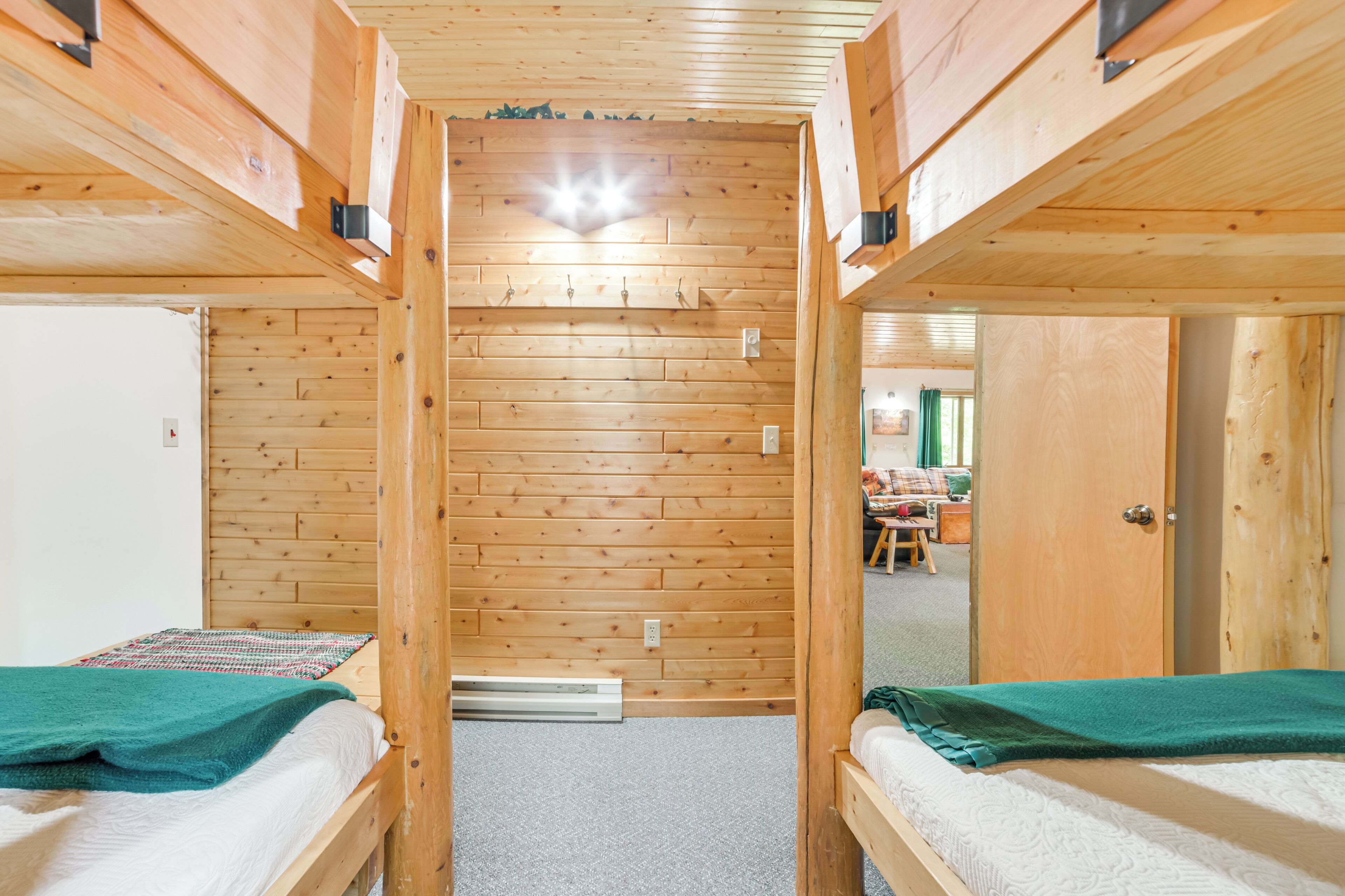 A room with two bunk beds, wooden walls, a small table, and a door leading to another room.