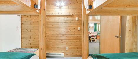 A room with two bunk beds, wooden walls, a small table, and a door leading to another room.