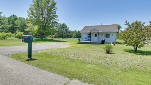 A small house with a porch, surrounded by a grassy yard and trees. - All-season Getaway in Frederic: Bring Your Pets! (Frederic)