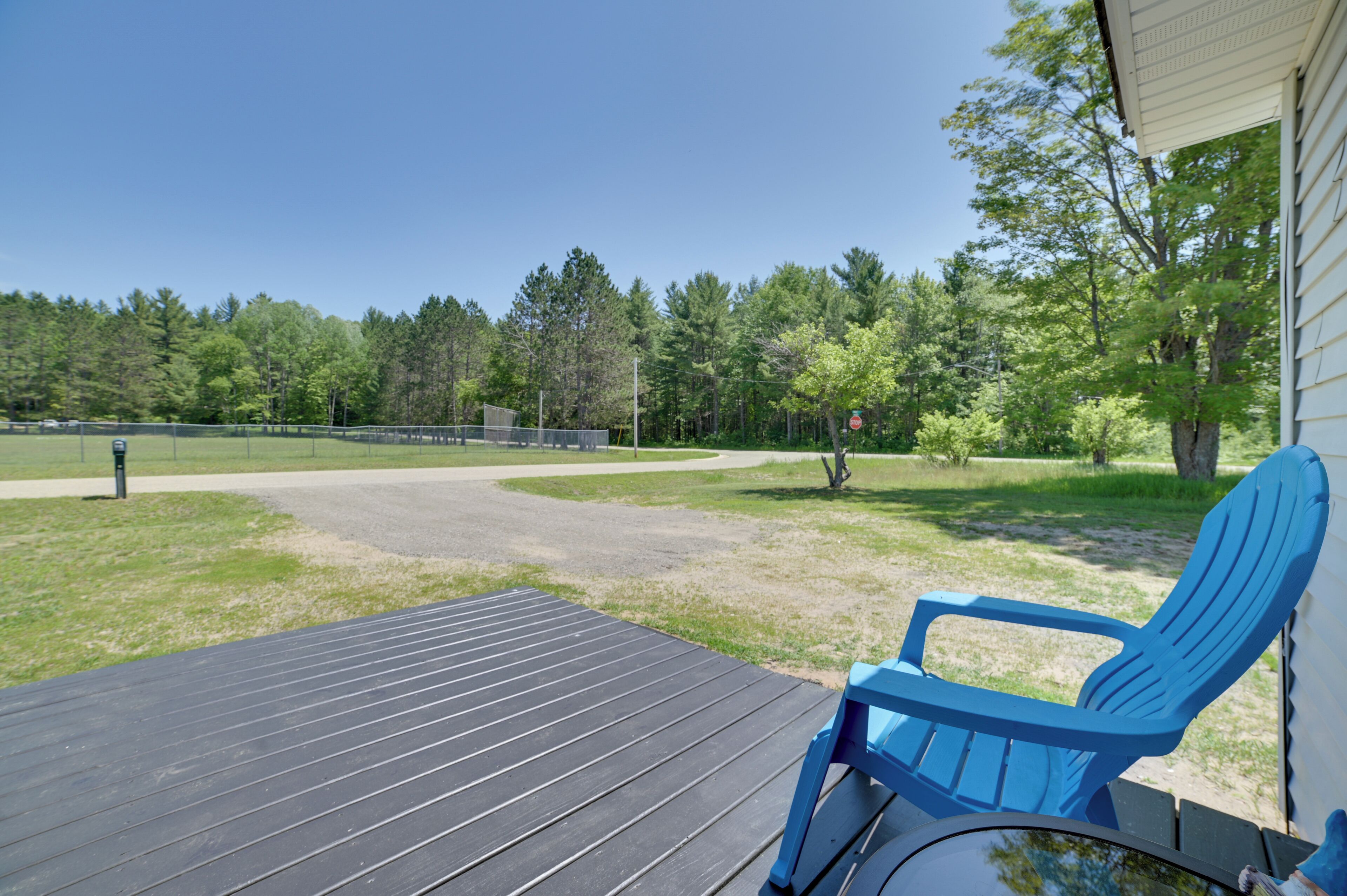 A wooden deck with a blue chair, a tennis court, and a forested area in the background.
