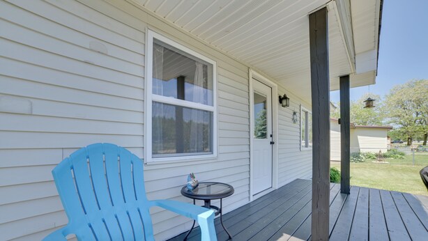 A porch with a blue Adirondack chair, a small round table, and a white door. - All-season Getaway in Frederic: Bring Your Pets! (Frederic)