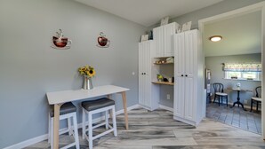 A kitchen with a white table and bar stools, a white cabinet, and a vase with sunflowers. - All-season Getaway in Frederic: Bring Your Pets! (Frederic)