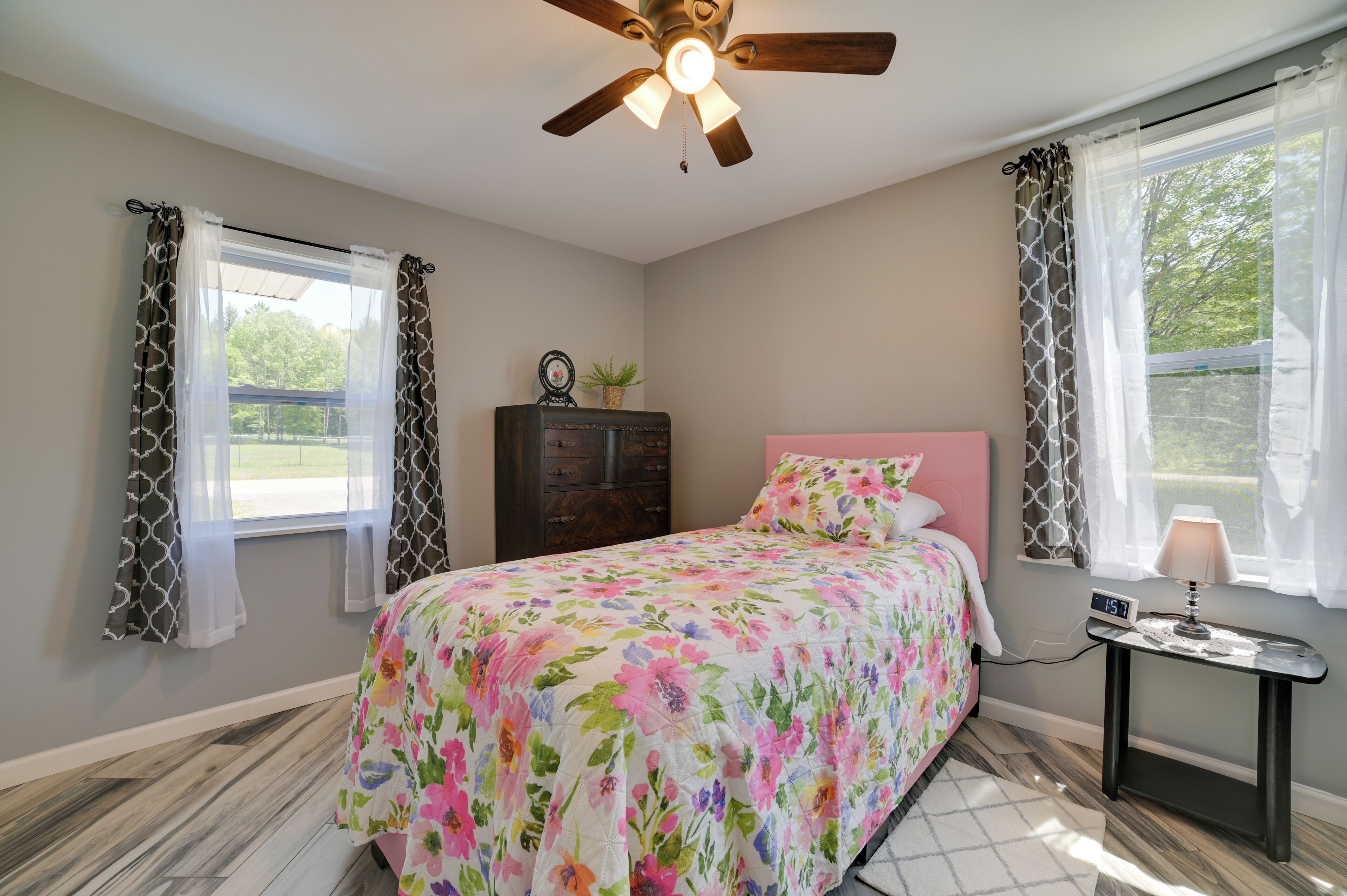 A bedroom with a bed, a ceiling fan, a dresser, and a bedside table with a lamp.