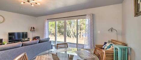A modern living room with a glass dining table, grey sofa, and a TV.