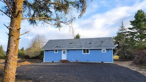 A single-story blue house with a front porch, a small front window, and a door with a wreath.
