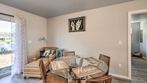 A dining area with a glass table and wooden chairs, a sofa with patterned cushions, and a framed artwork on the wall.