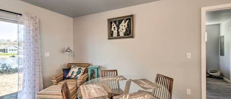 A dining area with a glass table and wooden chairs, a sofa with patterned cushions, and a framed artwork on the wall.