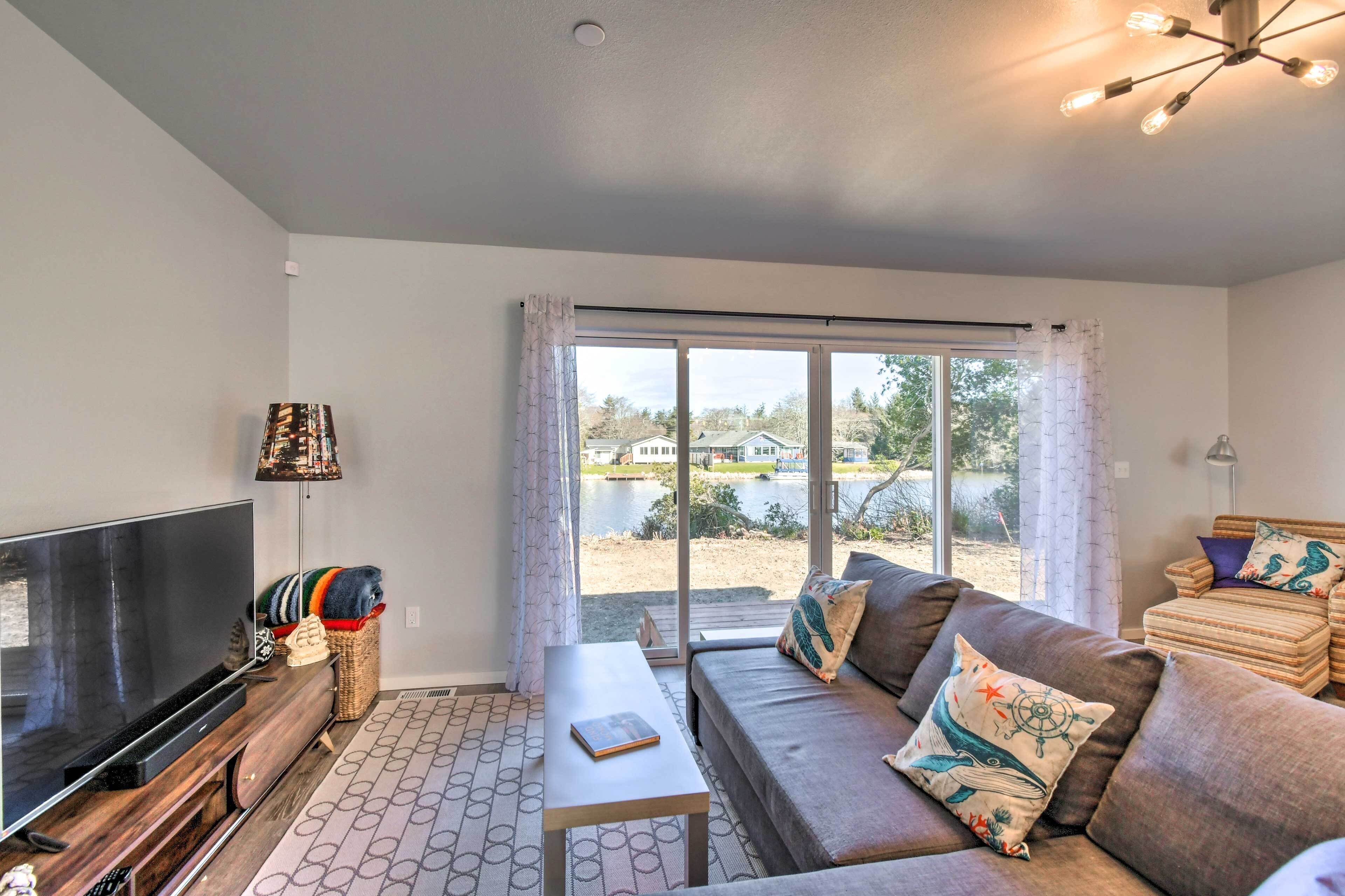 A modern living room with a flat-screen TV, sofa, and a view of a lake through large windows.