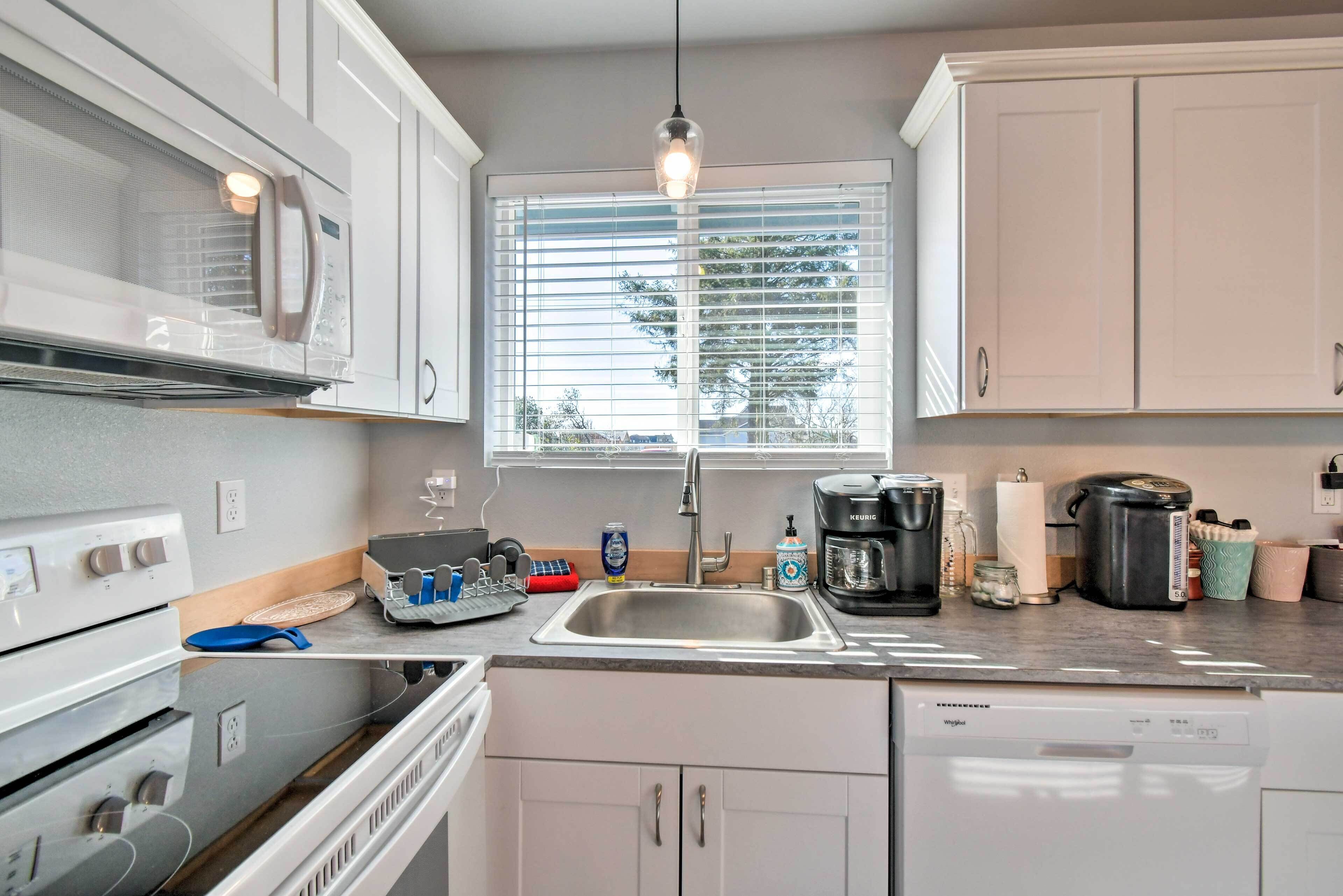 Una cocina moderna con gabinetes blancos, un lavamanos de acero inoxidable, una cafetera y un lavavajillas.
