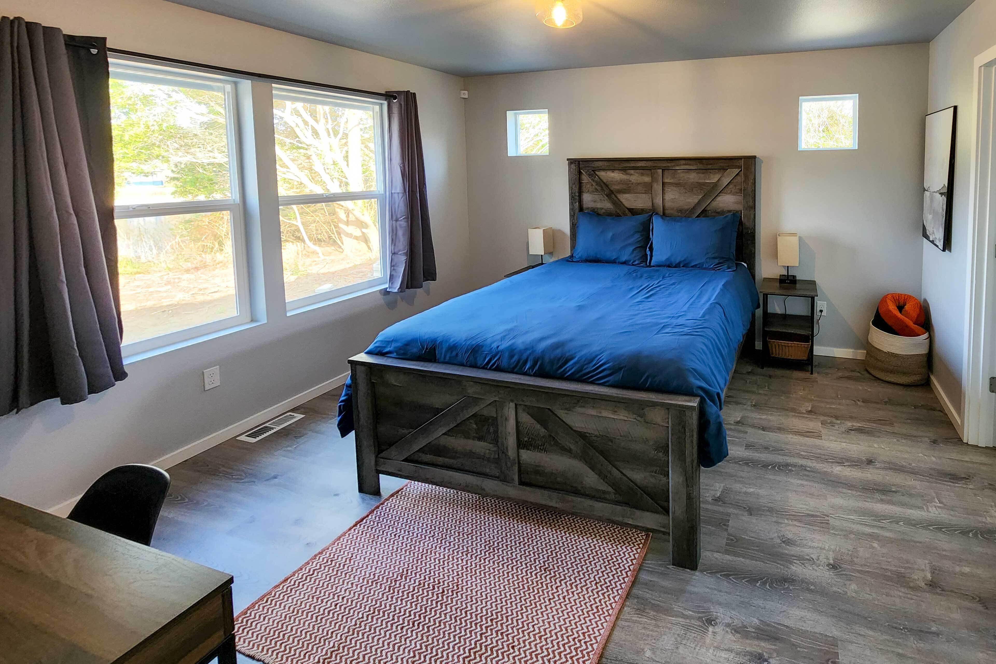 Une chambre à coucher avec un grand lit, une tête de lit en bois, un bureau et une fenêtre avec des rideaux.
