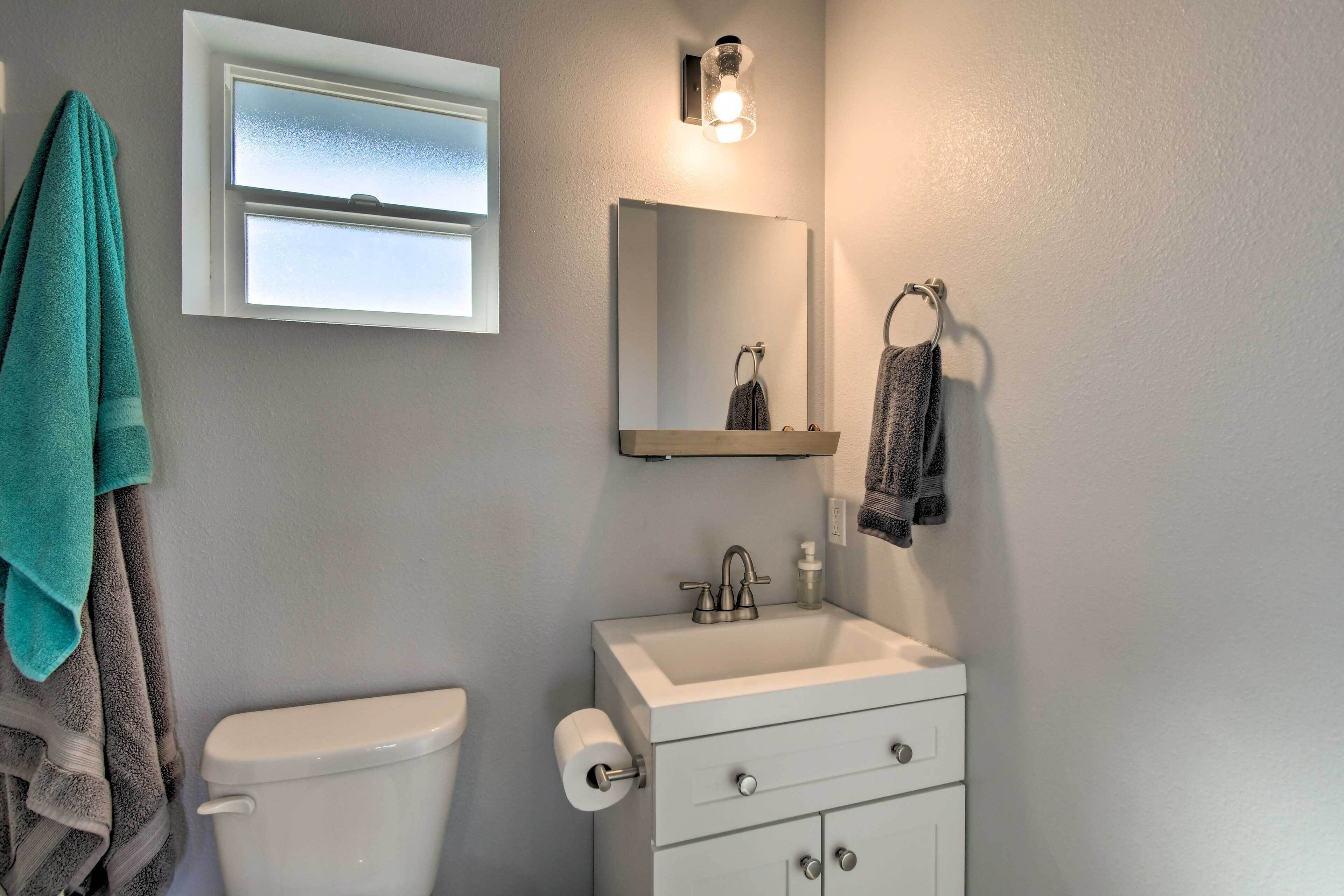 Un baño con inodoro, lavamanos, espejo, toallero y ventana.