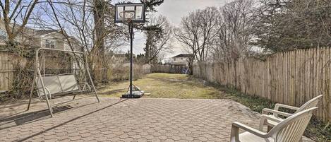 A hexagonal paved patio with a basketball hoop, a swing set, and a wooden fence in the background.