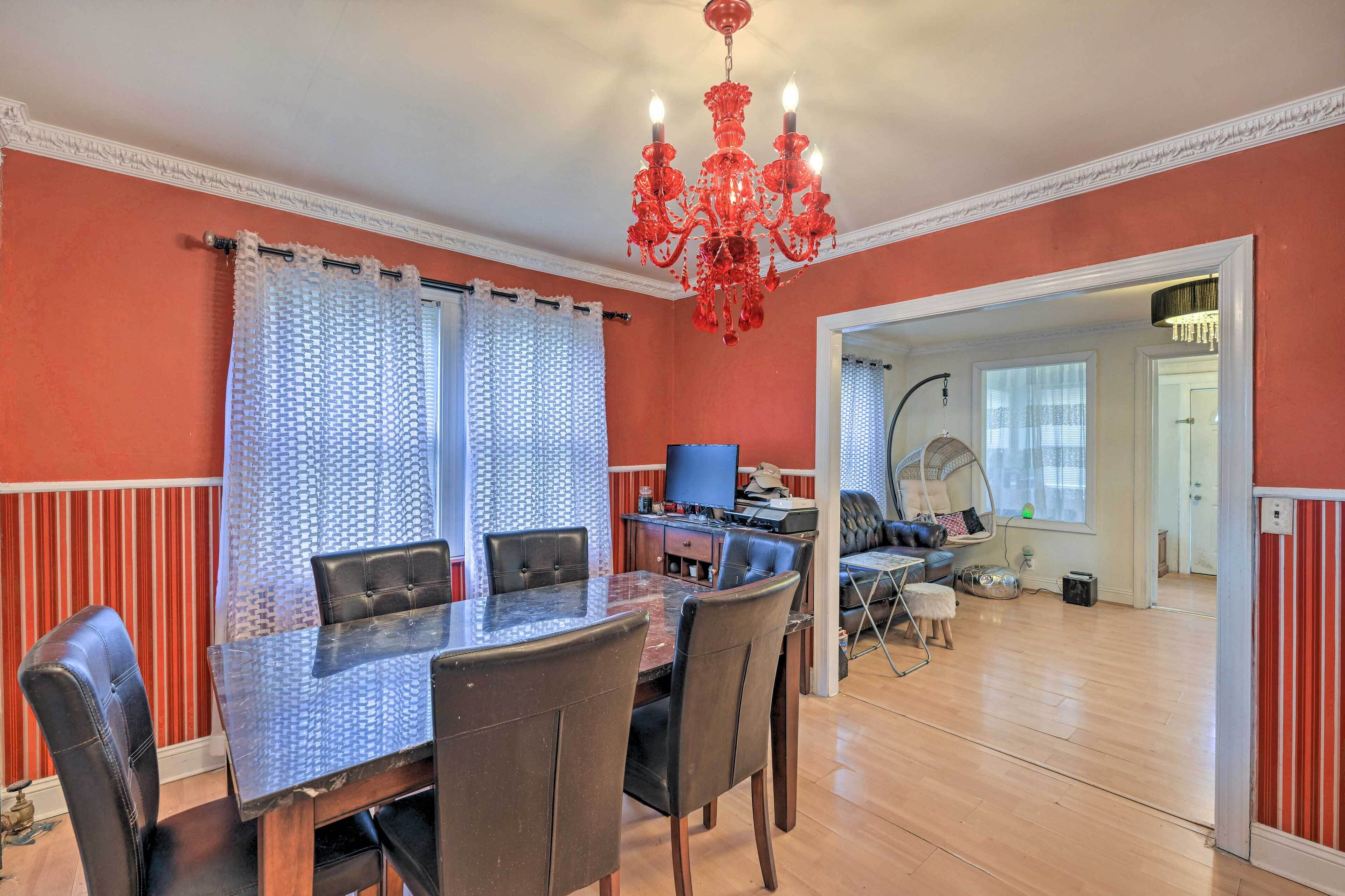 A dining area with a glass table and chairs, a red chandelier, and a television in the background.