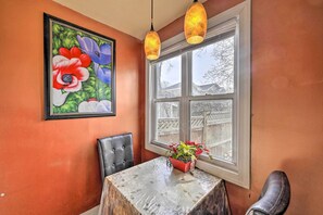 A dining area with a table, chairs, a potted plant, a framed painting, and a window with a view of a wooden fence. - Charming New York Escape Near Central Park! (Jericho)
