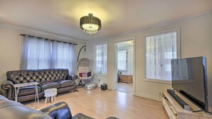 A living room with a leather sofa, a small table, a television, and a chandelier. - Charming New York Escape Near Central Park! (Jericho)