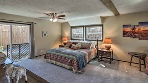 A bedroom with a large bed, a ceiling fan, a window with a view, a nightstand, and a small table. - Charming Texas Home w/ Stunning Canyon Views! (Canyon)