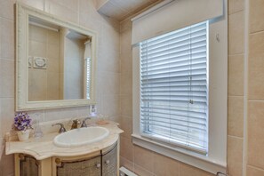 Un baño con lavamanos, espejo y ventana con persianas.