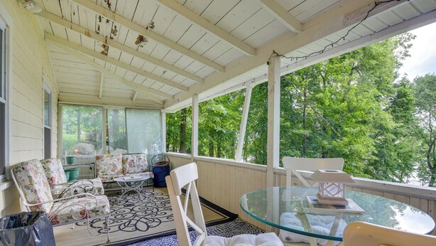 Une véranda avec des meubles blancs, une table en verre et une vue sur les arbres.