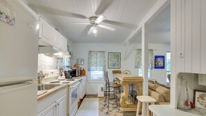 Une cuisine avec des armoires blanches, un plan de travail en bois, un ventilateur de plafond et un coin repas comprenant une table et des chaises.
