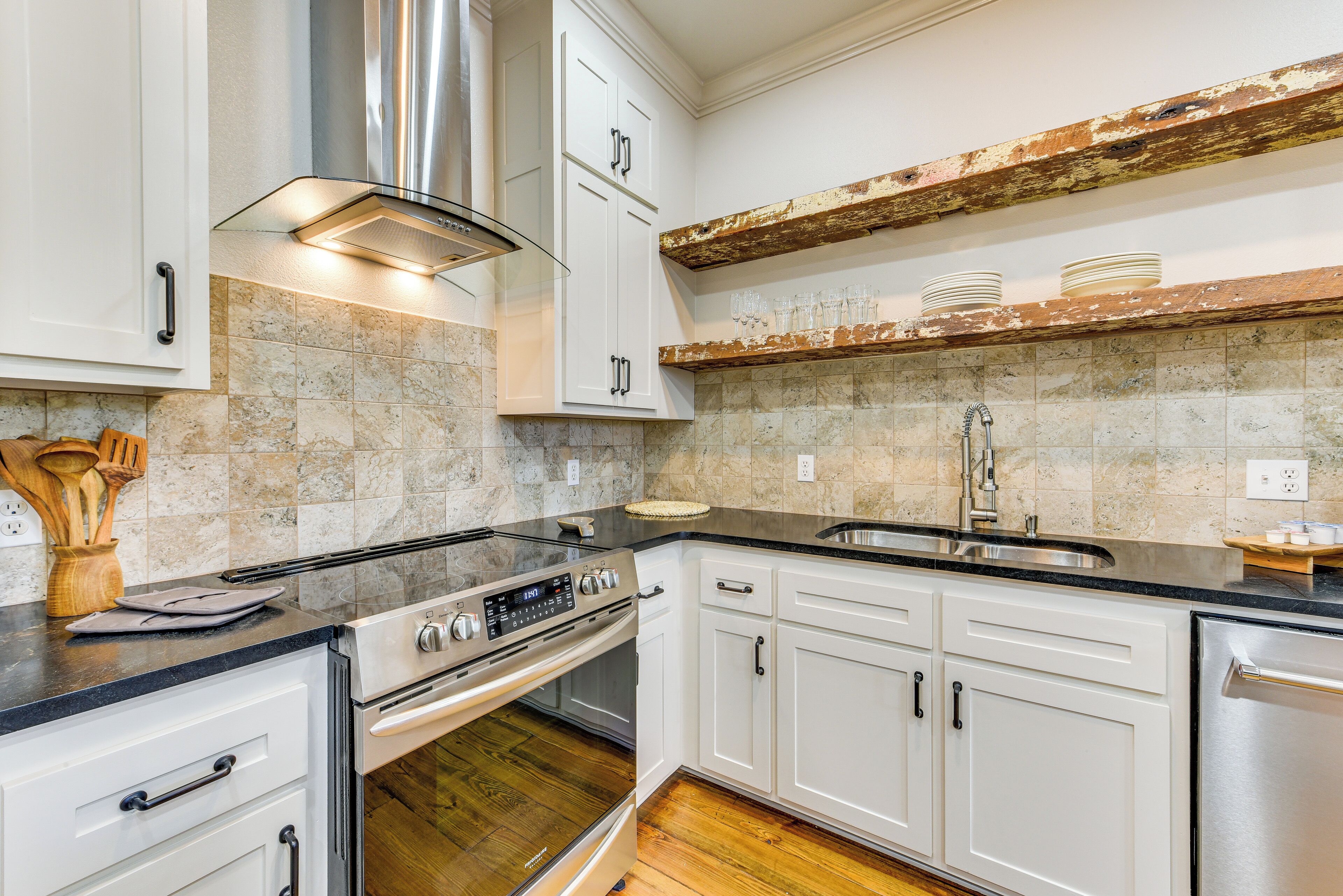 A modern kitchen with white cabinets, a stainless steel range hood, a built-in oven, and a dishwasher.
