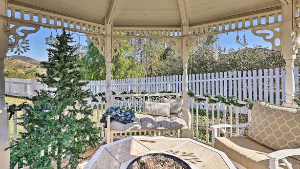 A covered patio with a white picket fence, a small Christmas tree, and a seating area with cushions and a fire pit. - Garden, Gazebo & Fire Pit: Fallbrook Home! (Fallbrook)