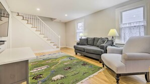 A living room with a staircase, a sofa, a chair, a lamp, and a rug. - Charming Hamden Home: 2 Mi to Yale University (Hamden)
