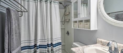 A bathroom with a shower curtain, a toilet, a sink, and a mirror.