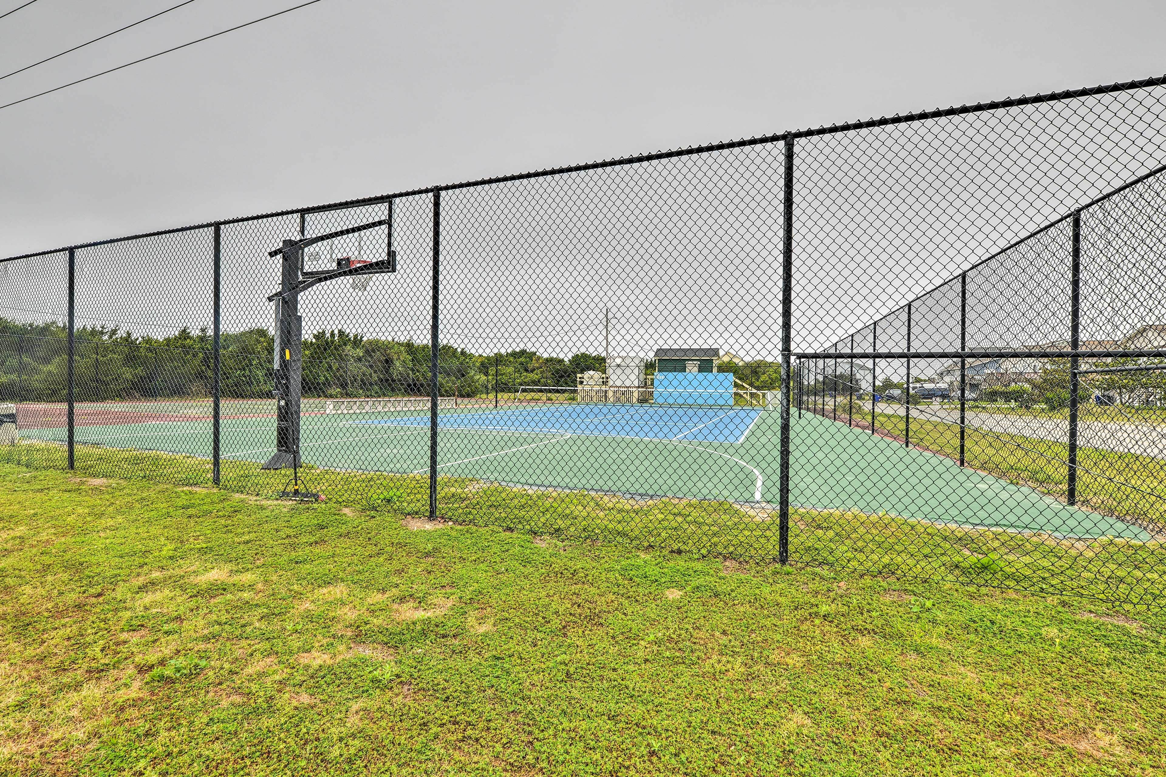 A fenced basketball court with a blue surface and a green area in the foreground.