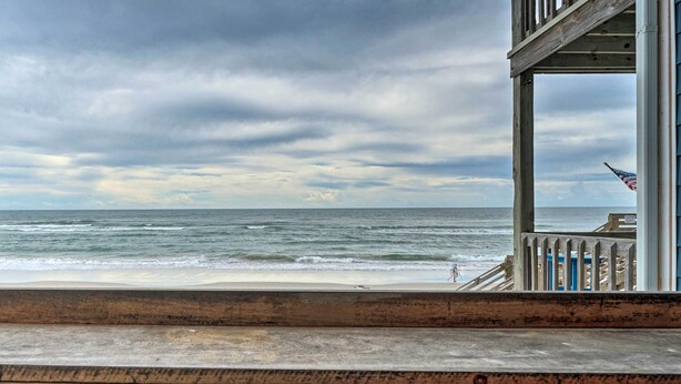 A wooden deck overlooking a beach with a view of the ocean and a cloudy sky.
