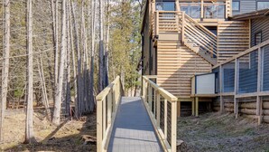 A wooden cabin with a wooden deck leading to the entrance, surrounded by trees. - Clam Lake Vacation Rental w/ Deck & Shared Dock! (Bellaire)