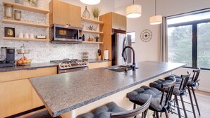 A modern kitchen with granite countertops, wooden cabinets, a stainless steel refrigerator, and a large island with bar stools. - Clam Lake Vacation Rental w/ Deck & Shared Dock! (Bellaire)