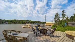 A wooden deck with outdoor furniture, a table, and a view of a lake and dock area. - Clam Lake Vacation Rental w/ Deck & Shared Dock! (Bellaire)