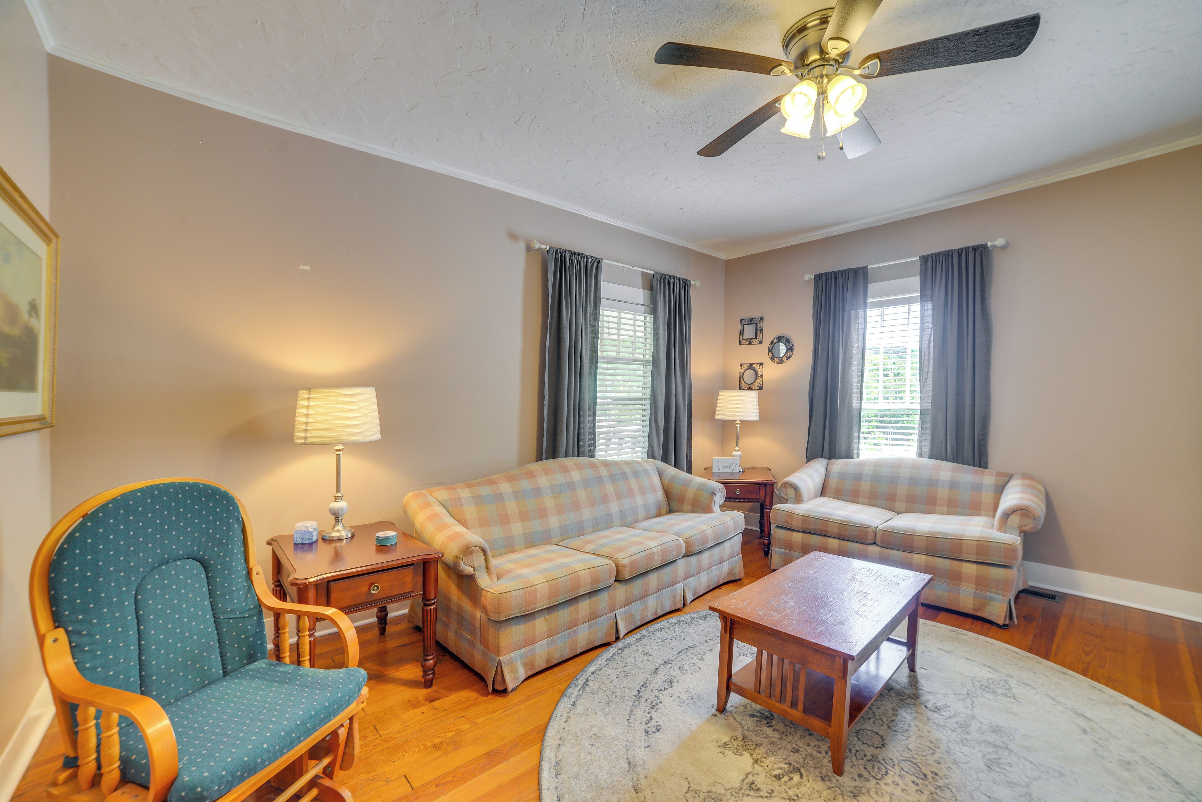A living room with a wooden floor, two sofas, a rocking chair, a coffee table, and a ceiling fan.