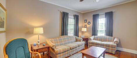 A living room with a wooden floor, two sofas, a rocking chair, a coffee table, and a ceiling fan.
