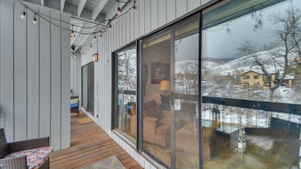 Un porche cubierto con terraza de madera, ventanas amplias y luces colgantes.