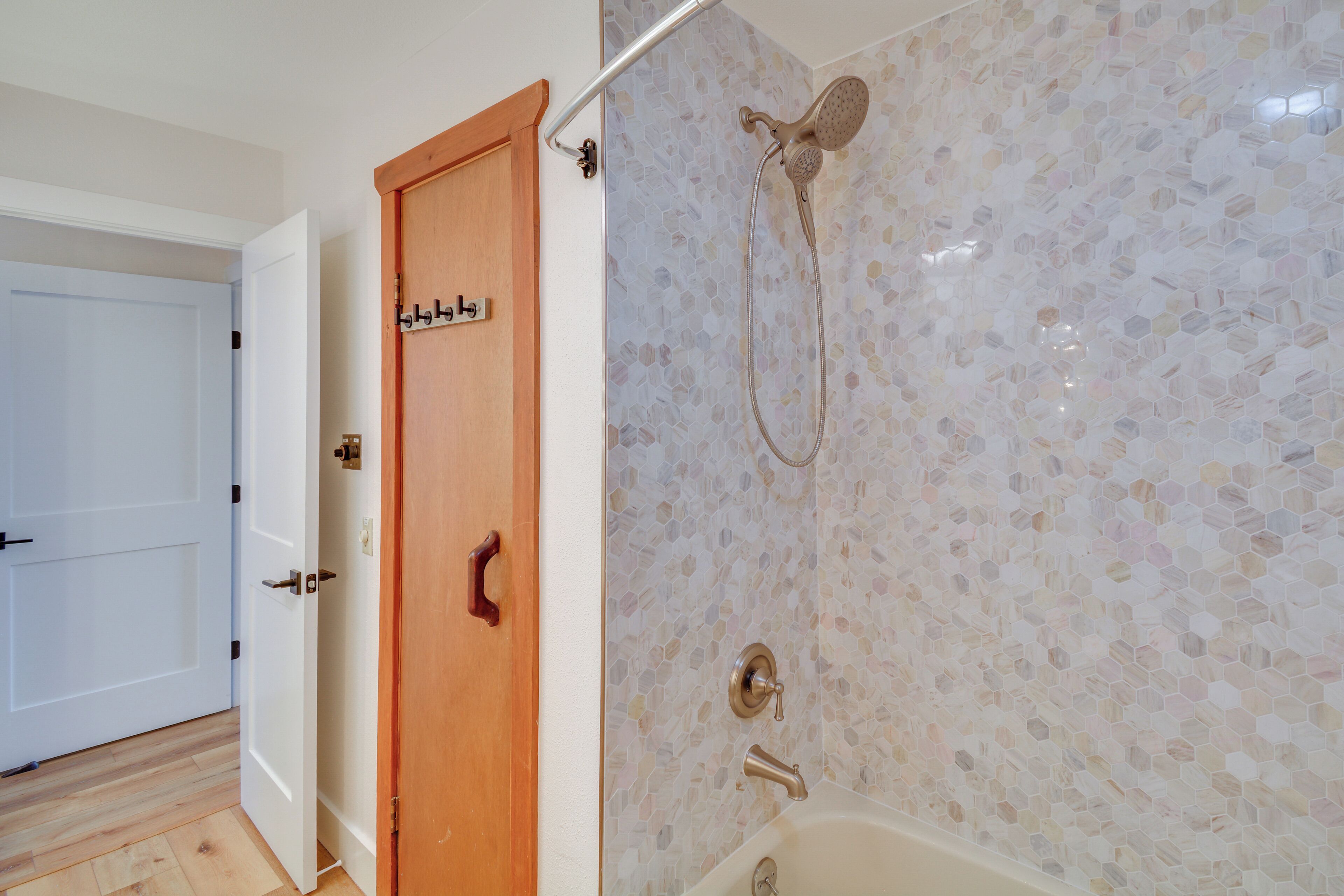 A bathroom with a shower, a wooden door, and a tiled wall.
