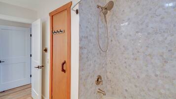 A bathroom with a shower, a wooden door, and a tiled wall.
