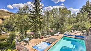 Una piscina con sillas de descanso y una mesa, rodeada de árboles y una montaña al fondo.